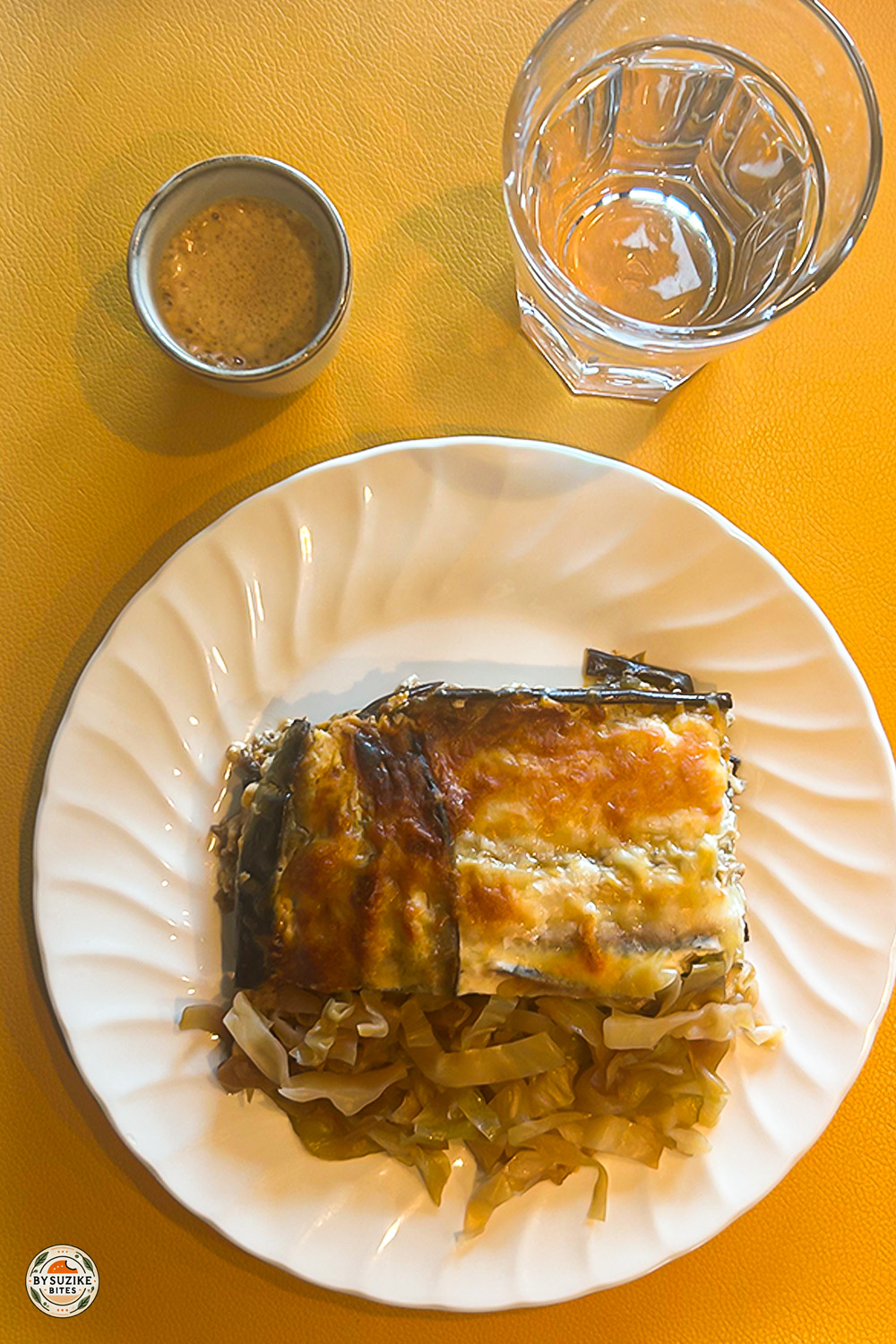 Eggplant lasagna with sautéed cabbage, espresso and water on white plate