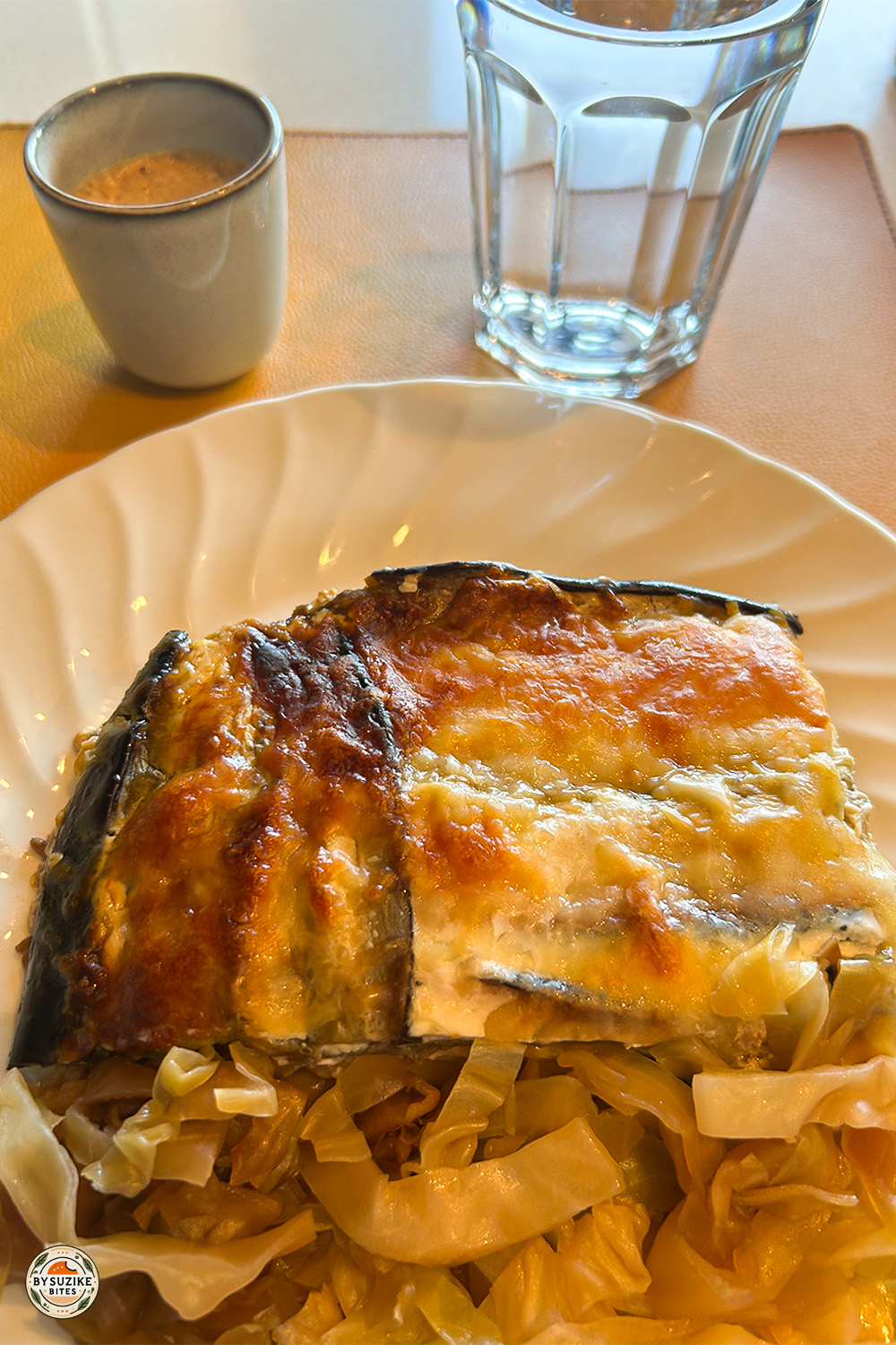 Eggplant lasagna with sautéed cabbage, espresso and water on white plate