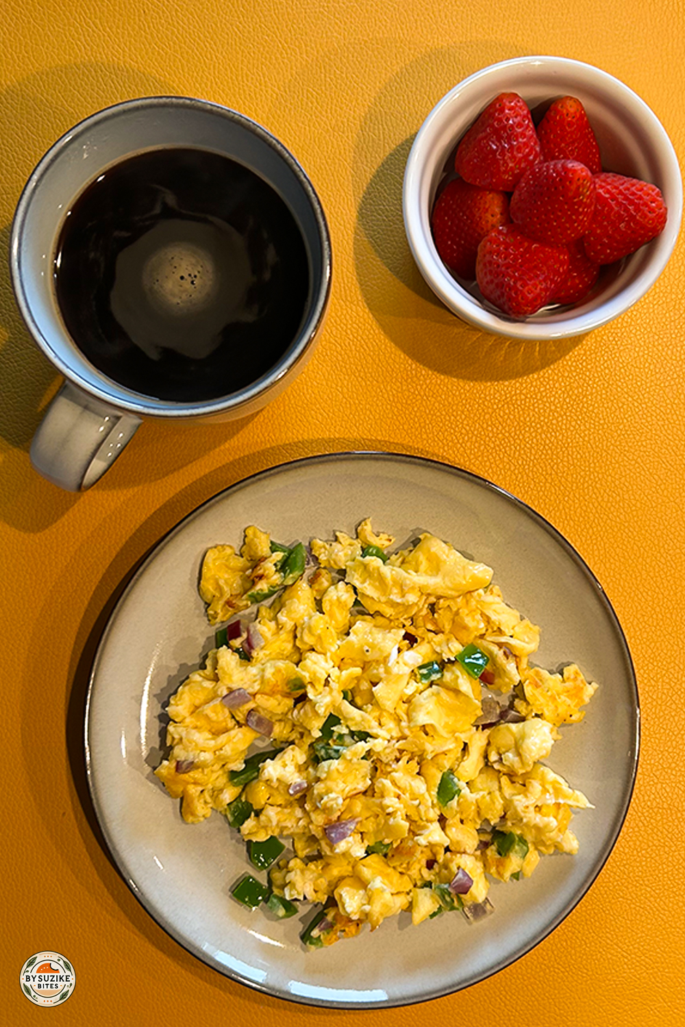 Low carb breakfast idea with scrambled eggs, black coffee, and strawberries on a yellow plate.