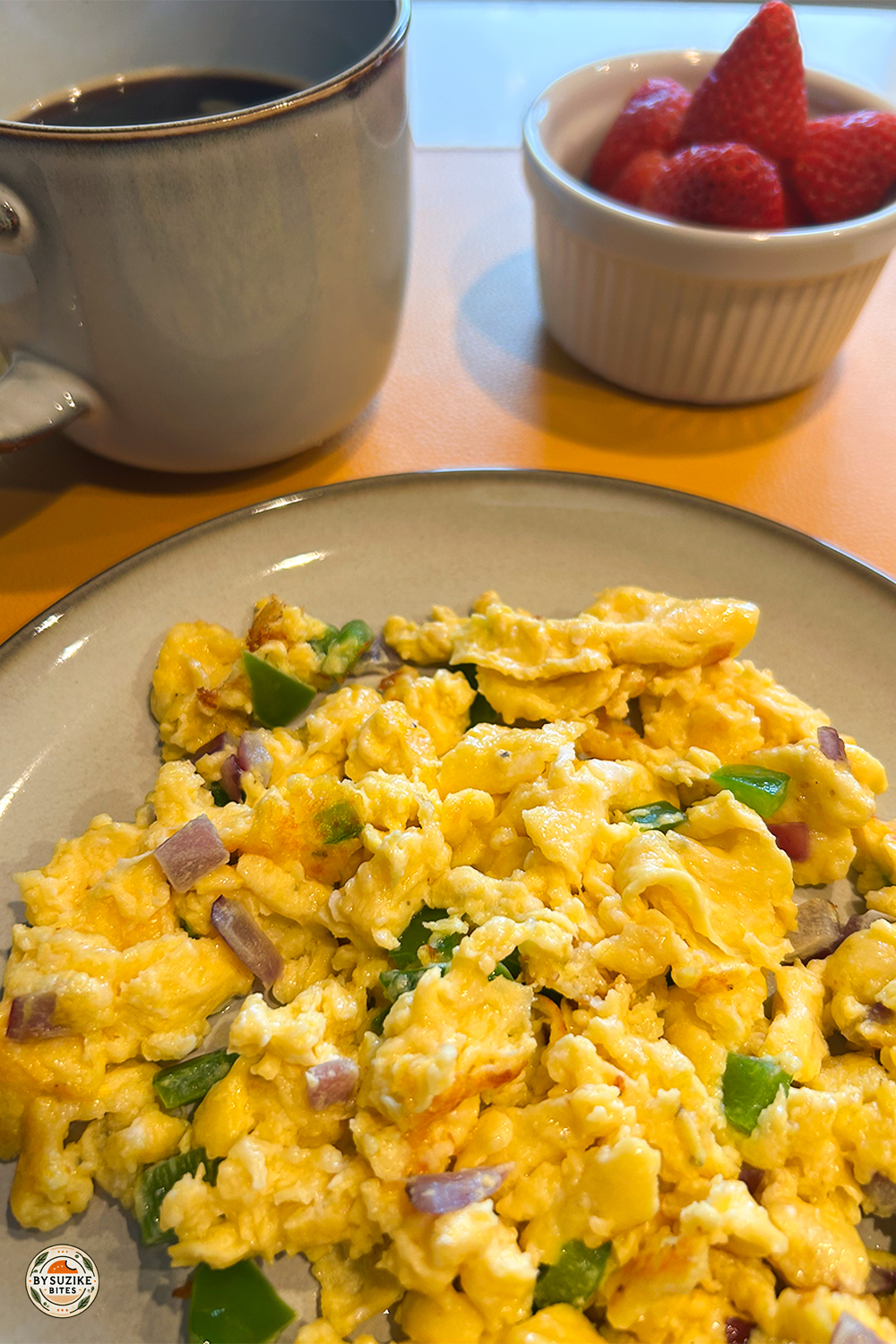 Low carb breakfast idea with scrambled eggs, black coffee, and strawberries on a yellow plate.