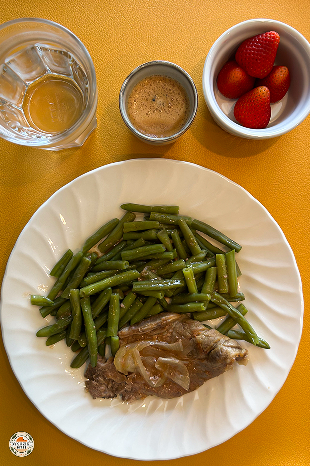 Low carb meal with pork chop, sautéed onions, green beans, fresh strawberries, espresso, and water on a white plate.