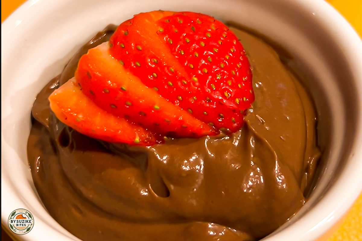Avocado chocolate mousse in a white ramekin topped with sliced strawberries – healthy low carb dessert.