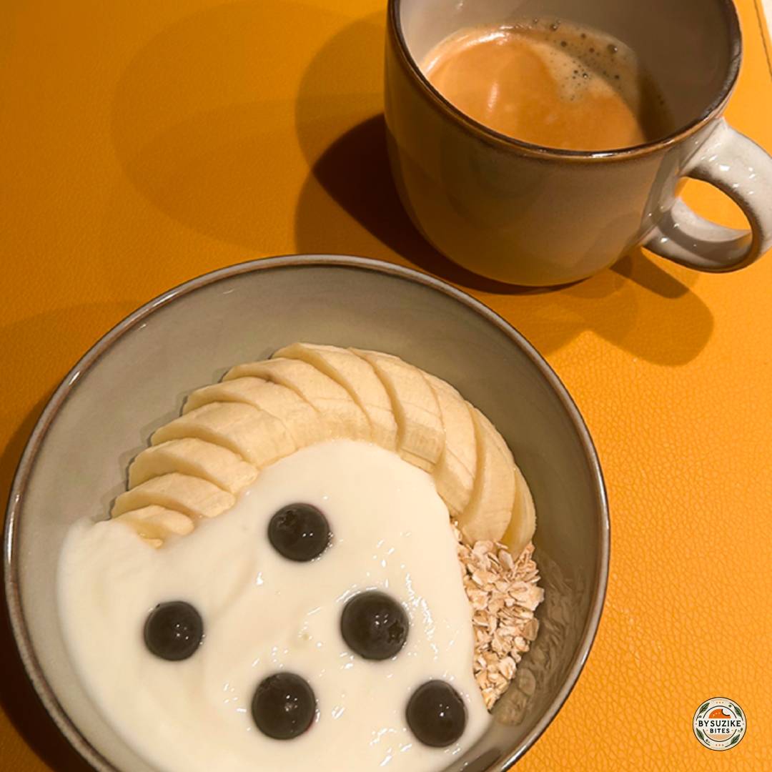 Mug of black coffee on an orange placemat, next to a breakfast bowl (partially visible)