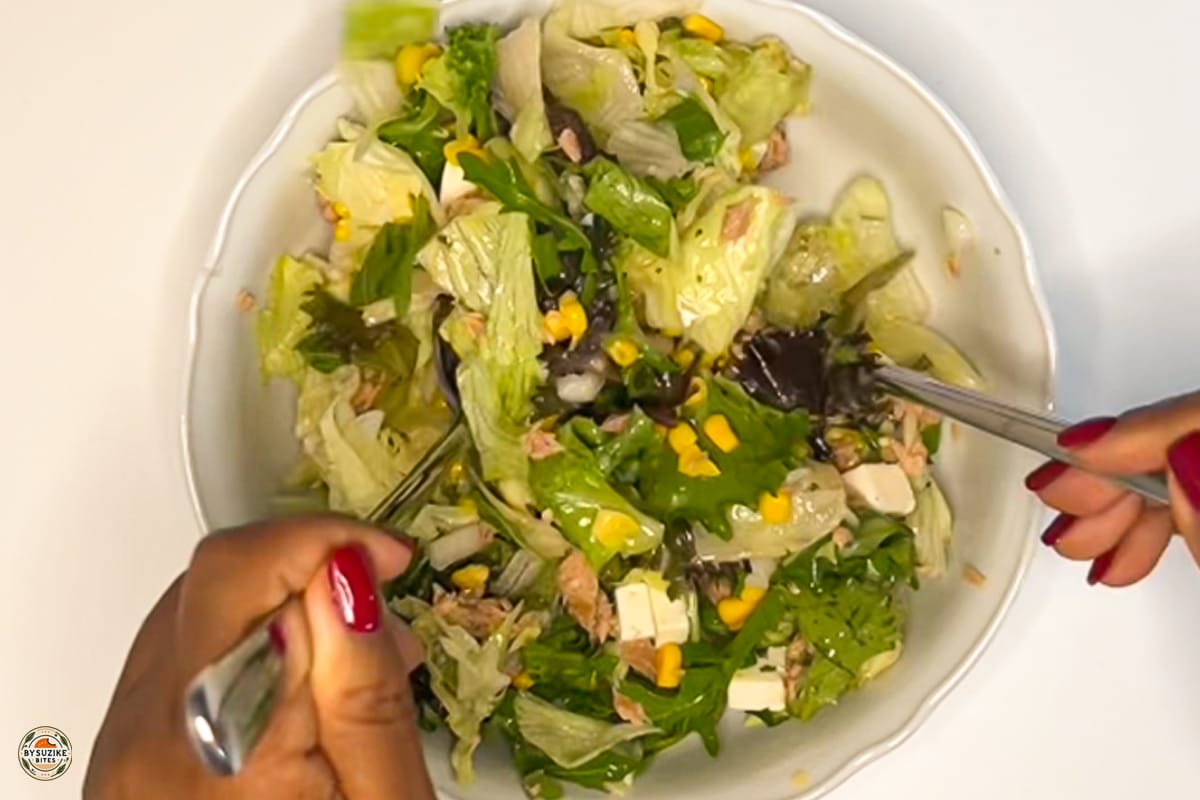 Feta and tuna salad with corn and red onion in a large bowl, drizzled with oregano vinaigrette