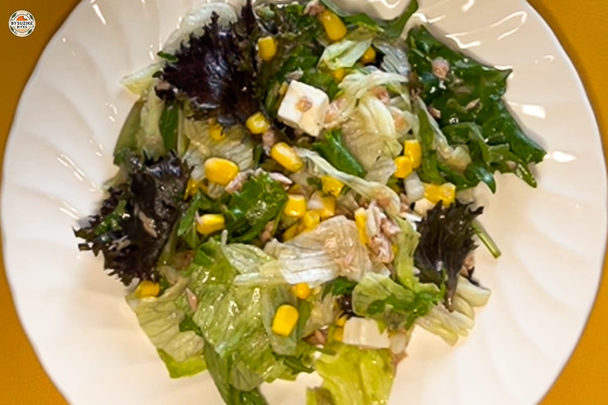 Feta and tuna salad with corn and red onion in a large bowl, drizzled with oregano vinaigrette