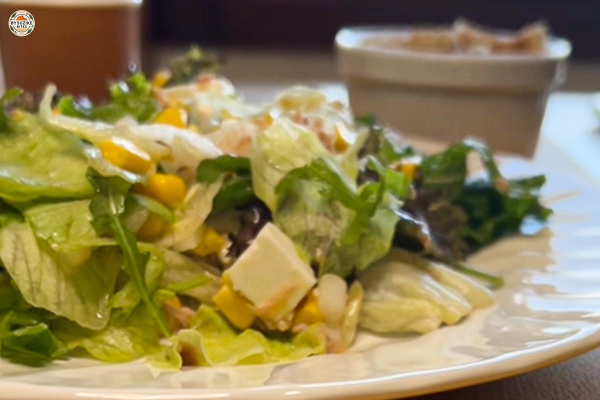 Feta and tuna salad with corn and red onion in a large bowl, drizzled with oregano vinaigrette