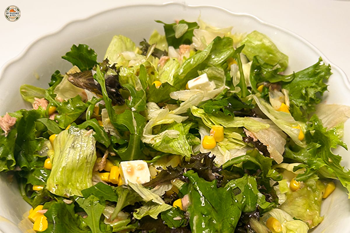 Feta and tuna salad with corn and red onion in a large bowl, drizzled with oregano vinaigrette