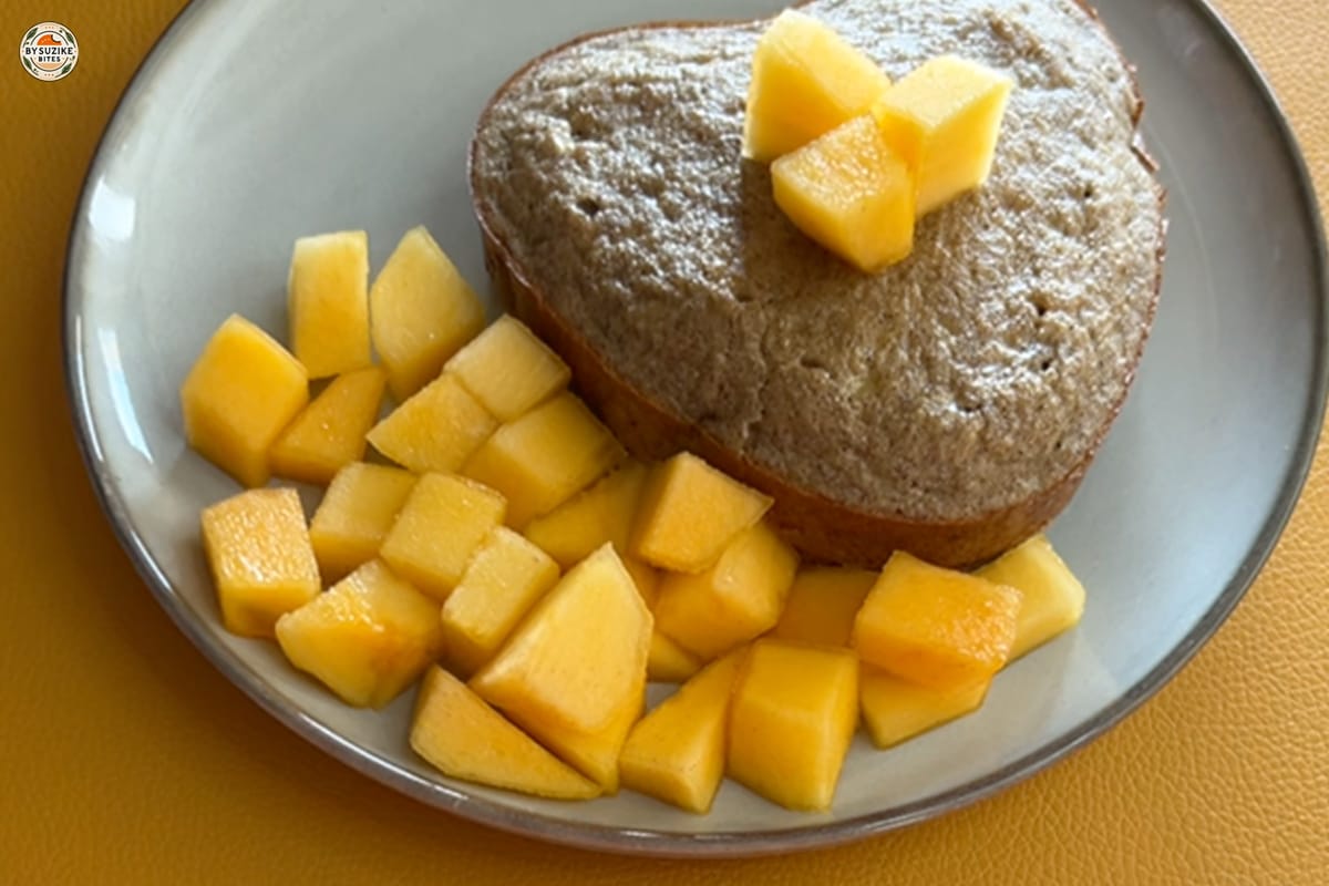 Oat Banana Cake 11 Heart-shaped banana oat cake served with fresh mango cubes on a gray plate over a yellow background.