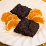 Healthy vegan banana brownies served with orange slices on a white plate