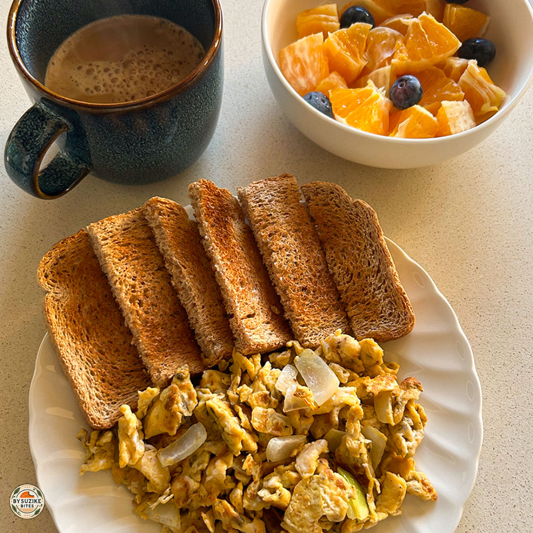 Plate of scrambled eggs with onions, whole wheat toast, a bowl of orange and blueberries, and a cup of coffee — easy scrambled eggs toast breakfast